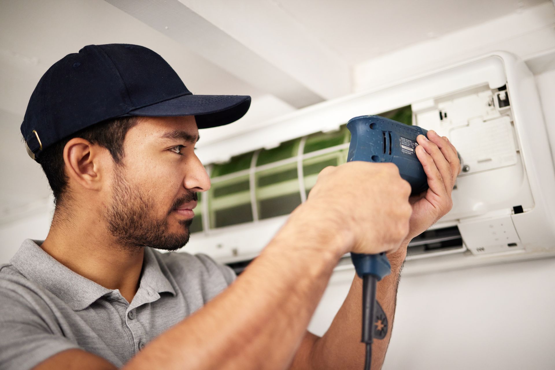 A man is fixing an air conditioner with a drill.
