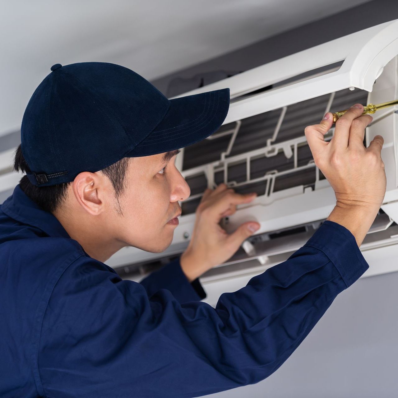 A man wearing a hat is working on an air conditioner