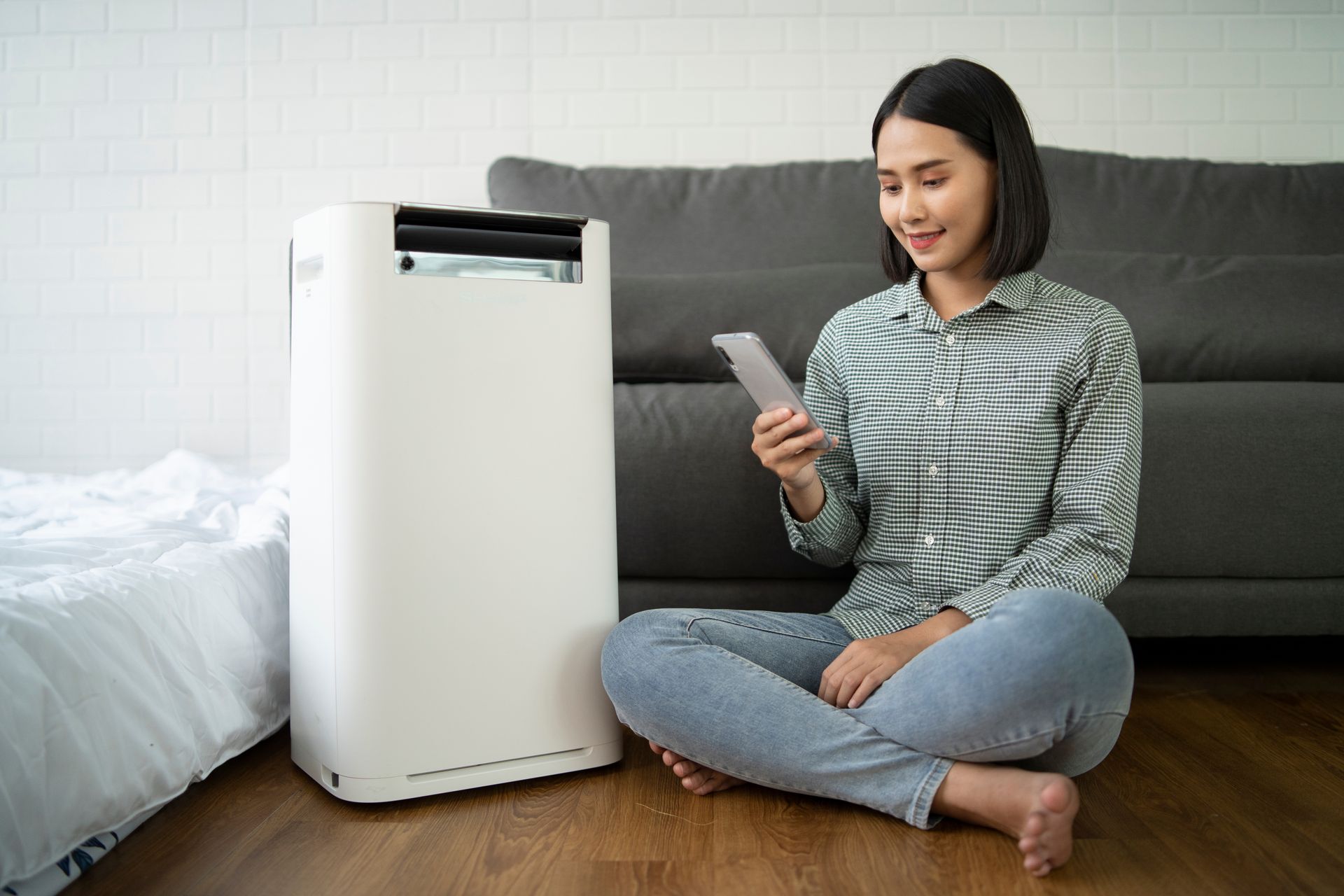 A woman is sitting on the floor using a tablet next to an air purifier.