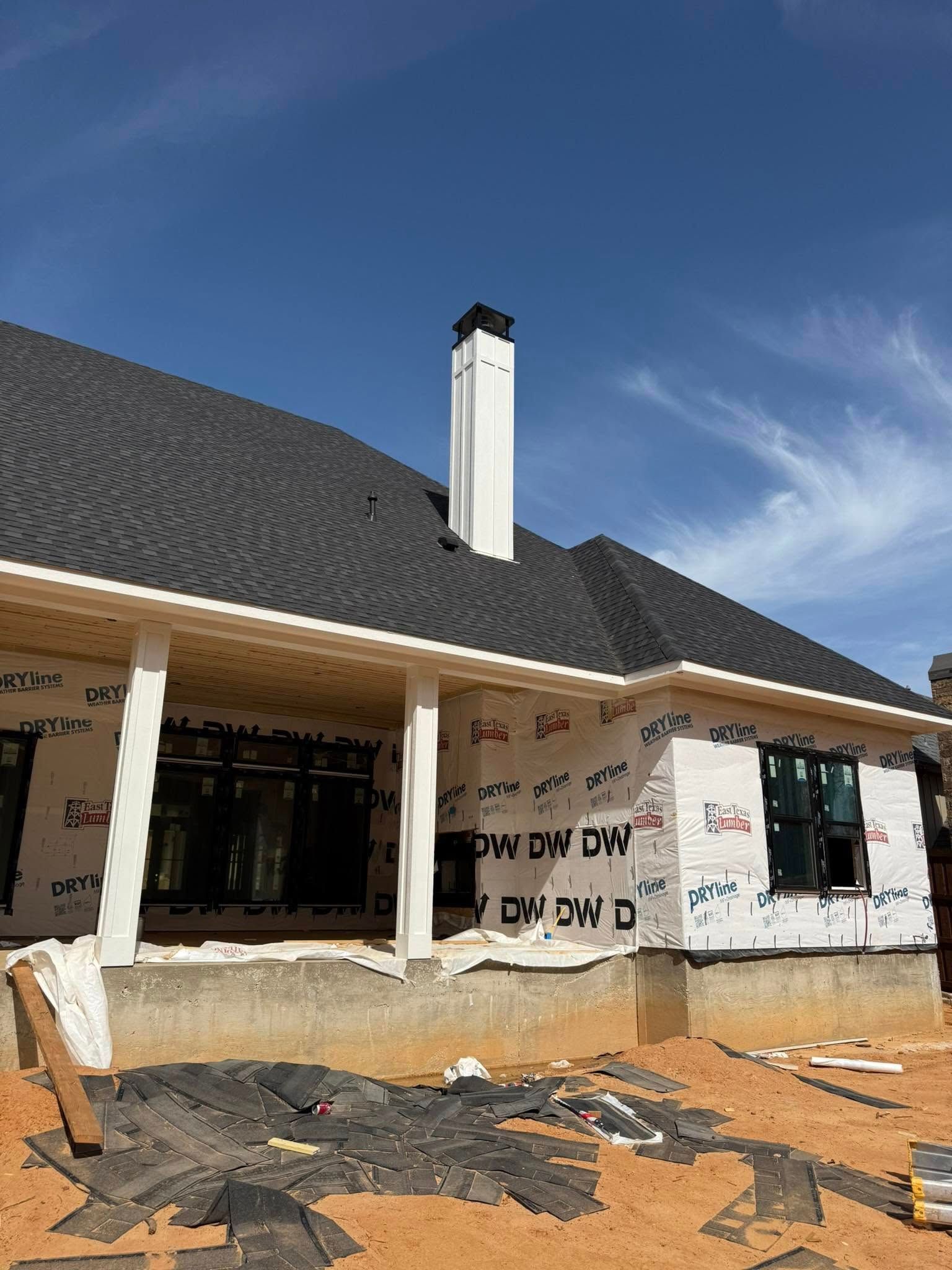 Construction site with a house under construction; dark roof, white chimney, blue sky.