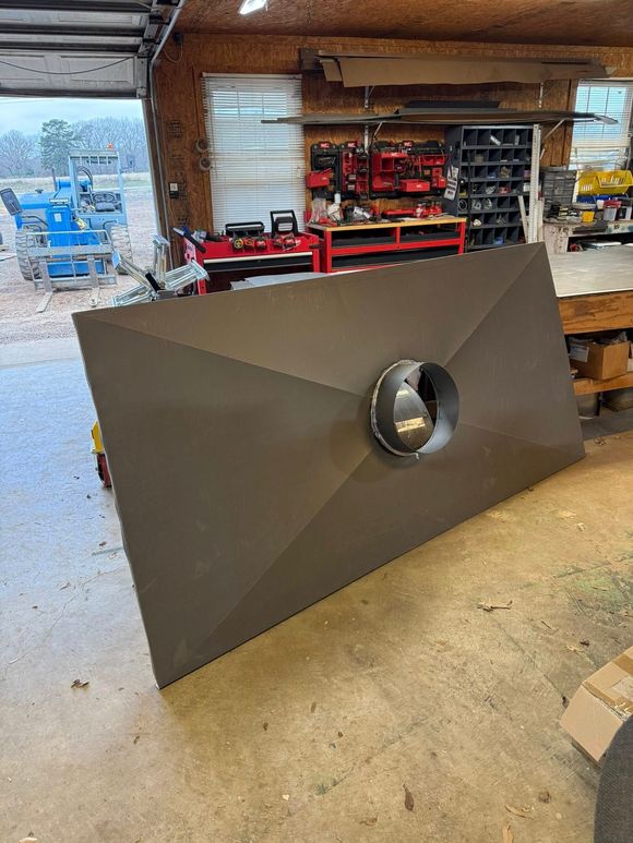 Large gray metal rectangular object with a circular hole in a workshop.