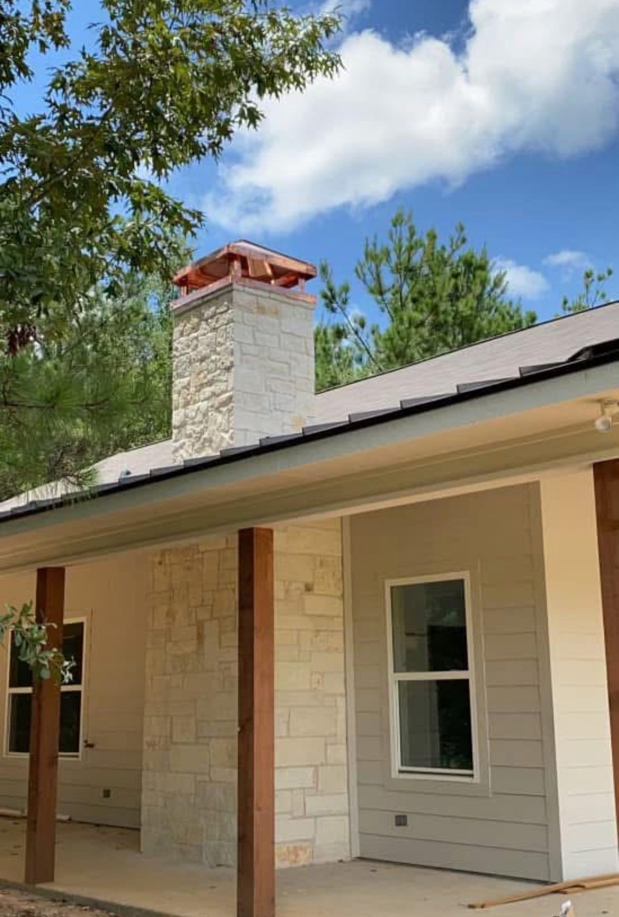 House exterior with stone chimney, gray siding, wood posts, and blue sky.