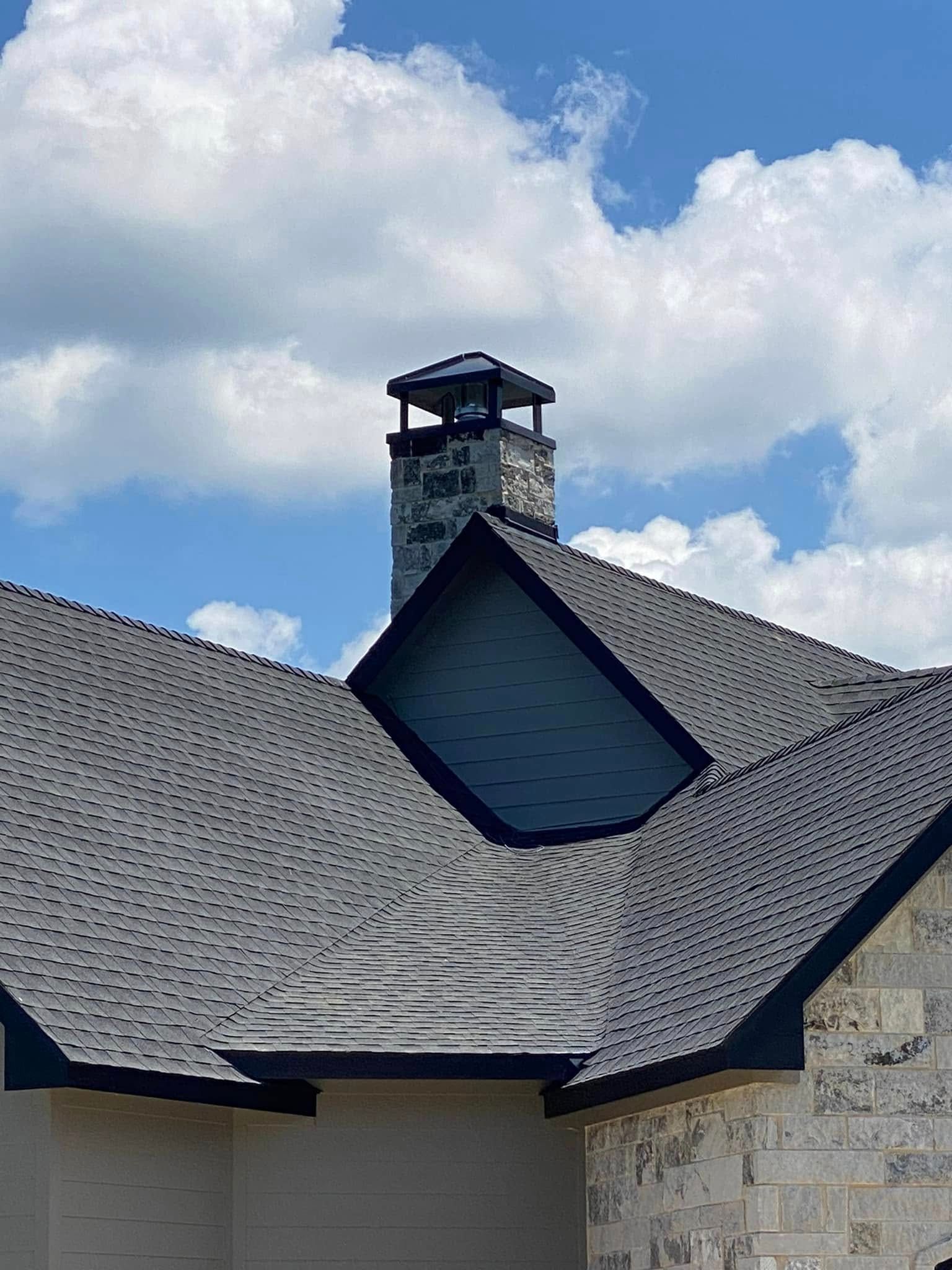 Chimney on a house with a grey shingle roof, blue sky, and white clouds.