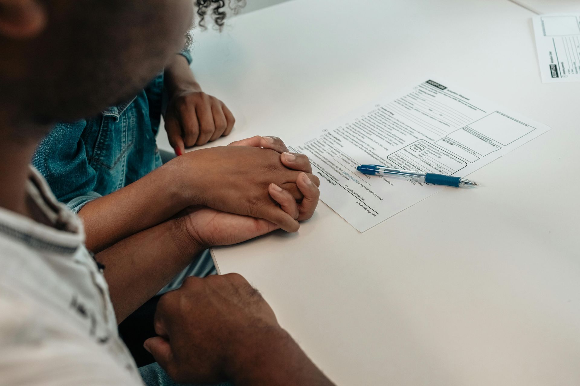 Hands on a table beside a worksheet and blue pen in a bright room