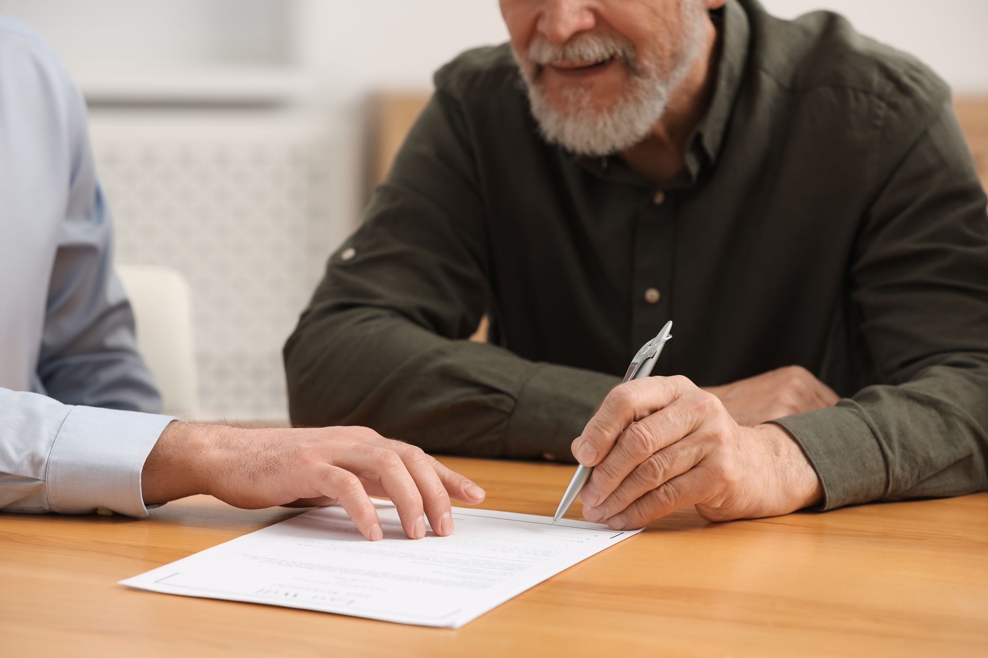 Two people reviewing a document at a wooden table, one pointing while another writes with a pen.