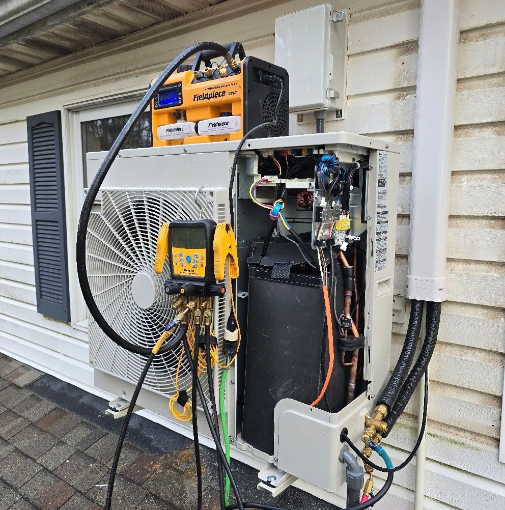 HVAC unit with open panel for repair. Tools and wires are connected. Outside, near house siding.