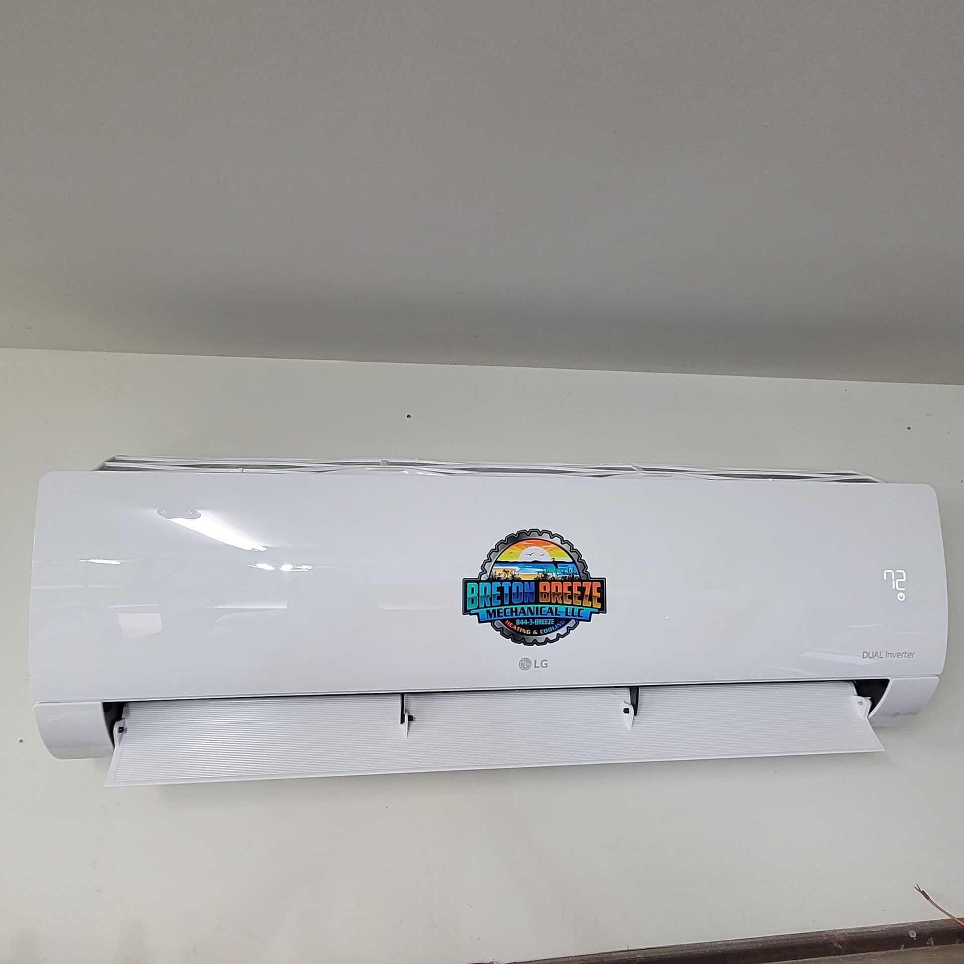 White air conditioner unit mounted on a white wall; colorful logo on the front.