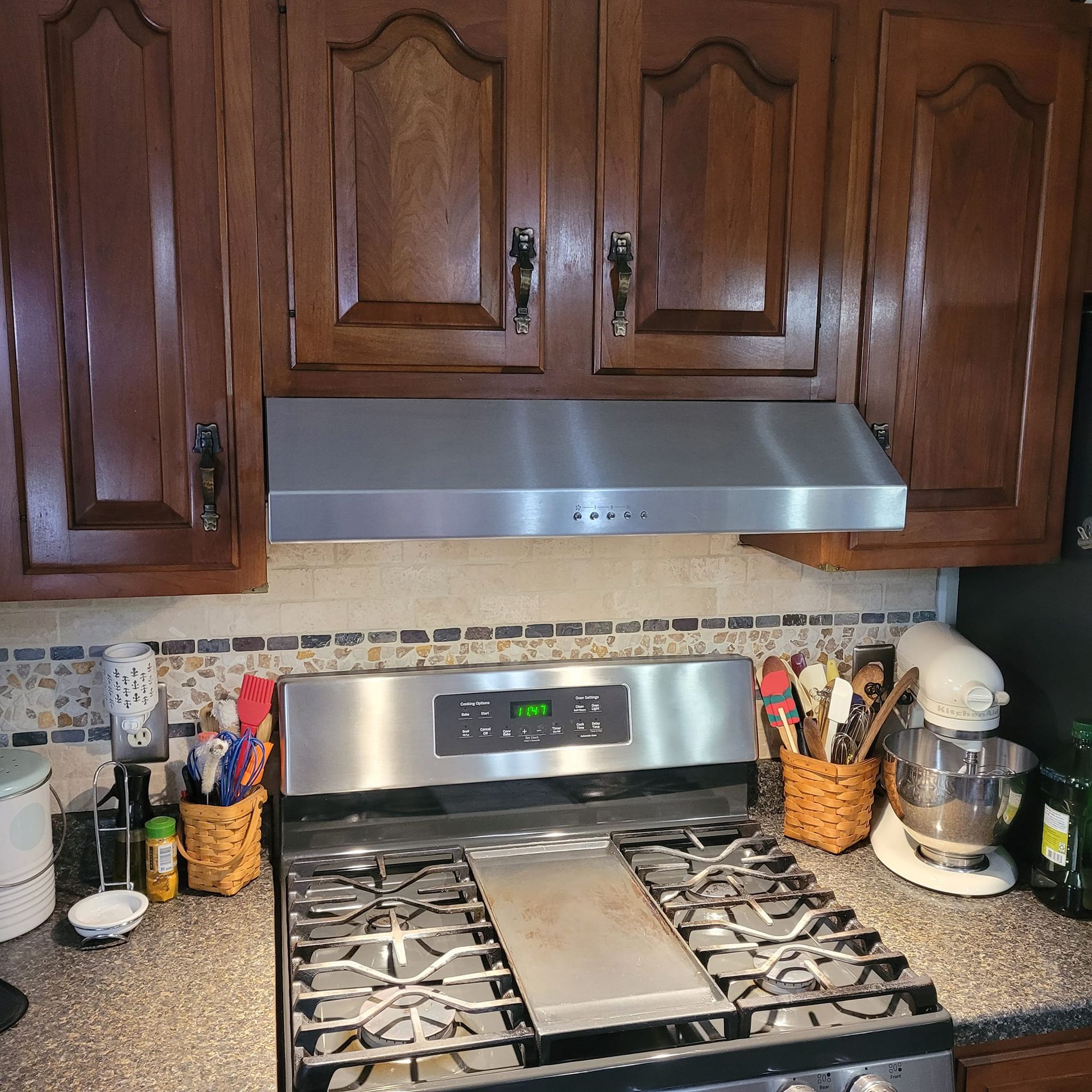 Kitchen with stainless steel stove and range hood, dark wood cabinets, and backsplash.