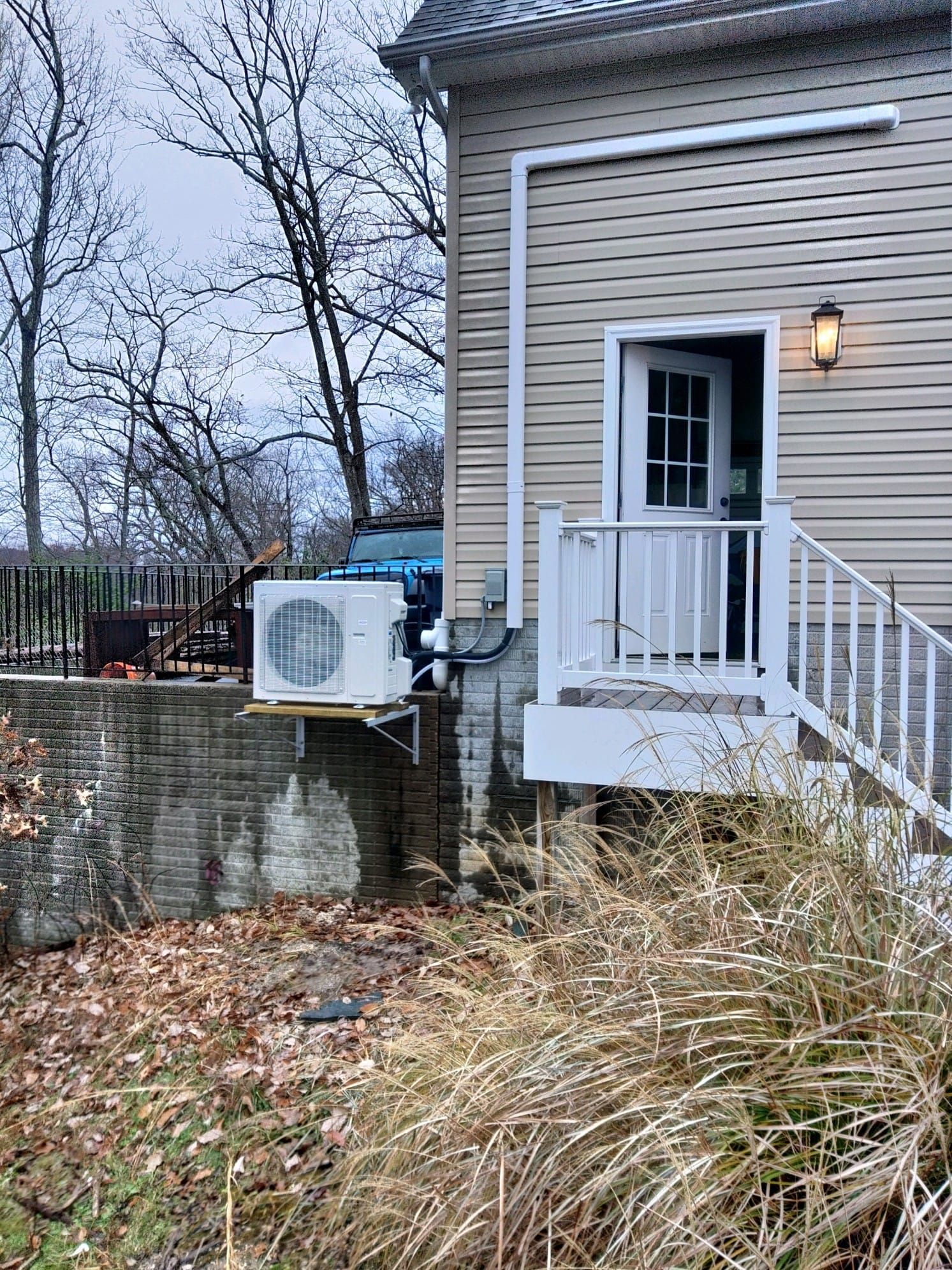 Exterior of a house with an air conditioning unit mounted on a brick wall. A white door and stairs are visible.