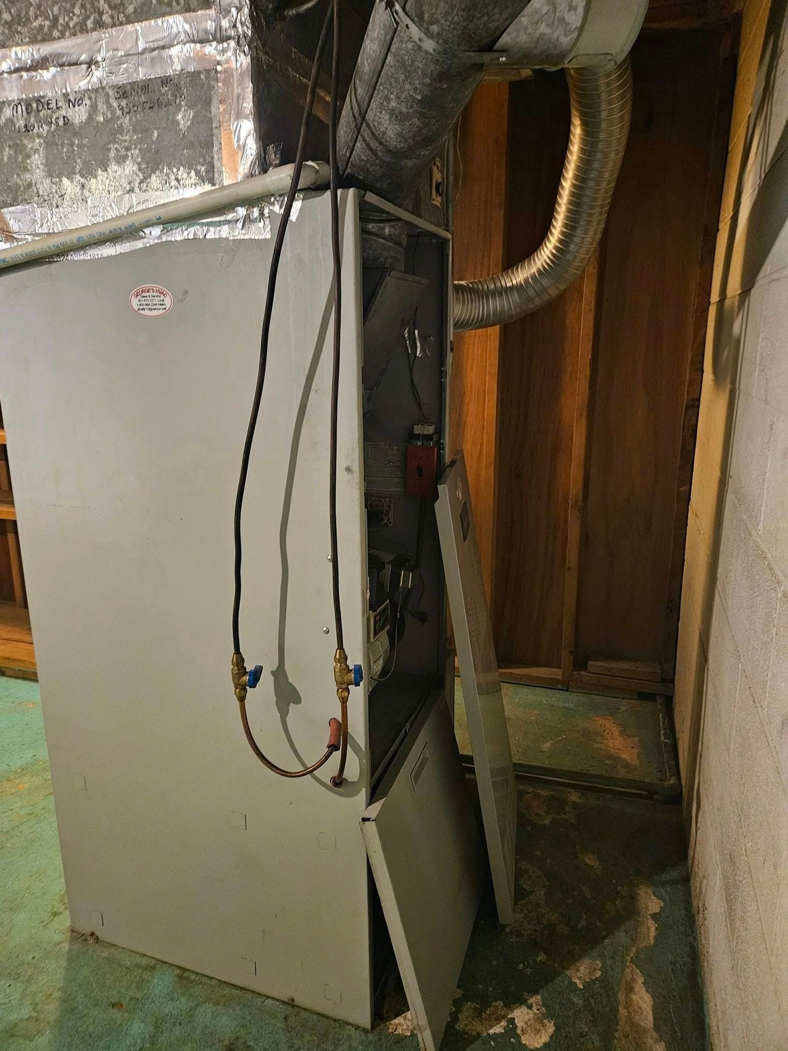 Furnace with open panels in a utility room; gray metal, exposed components, ductwork overhead.