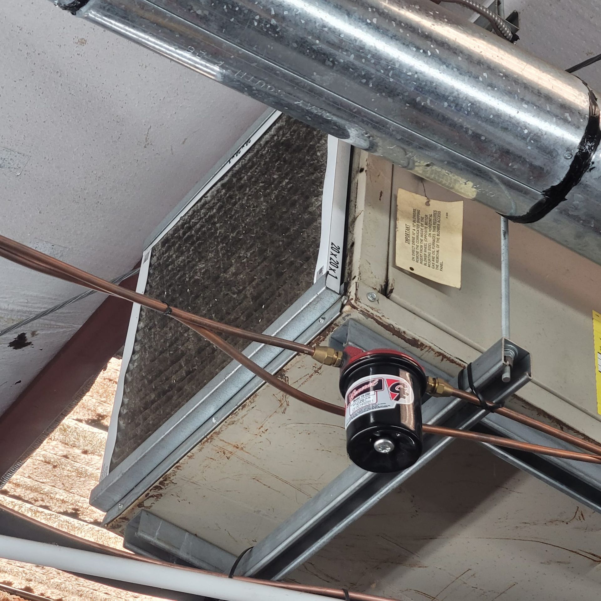 A dirty HVAC unit with copper pipes and a condensate pump attached to ductwork.