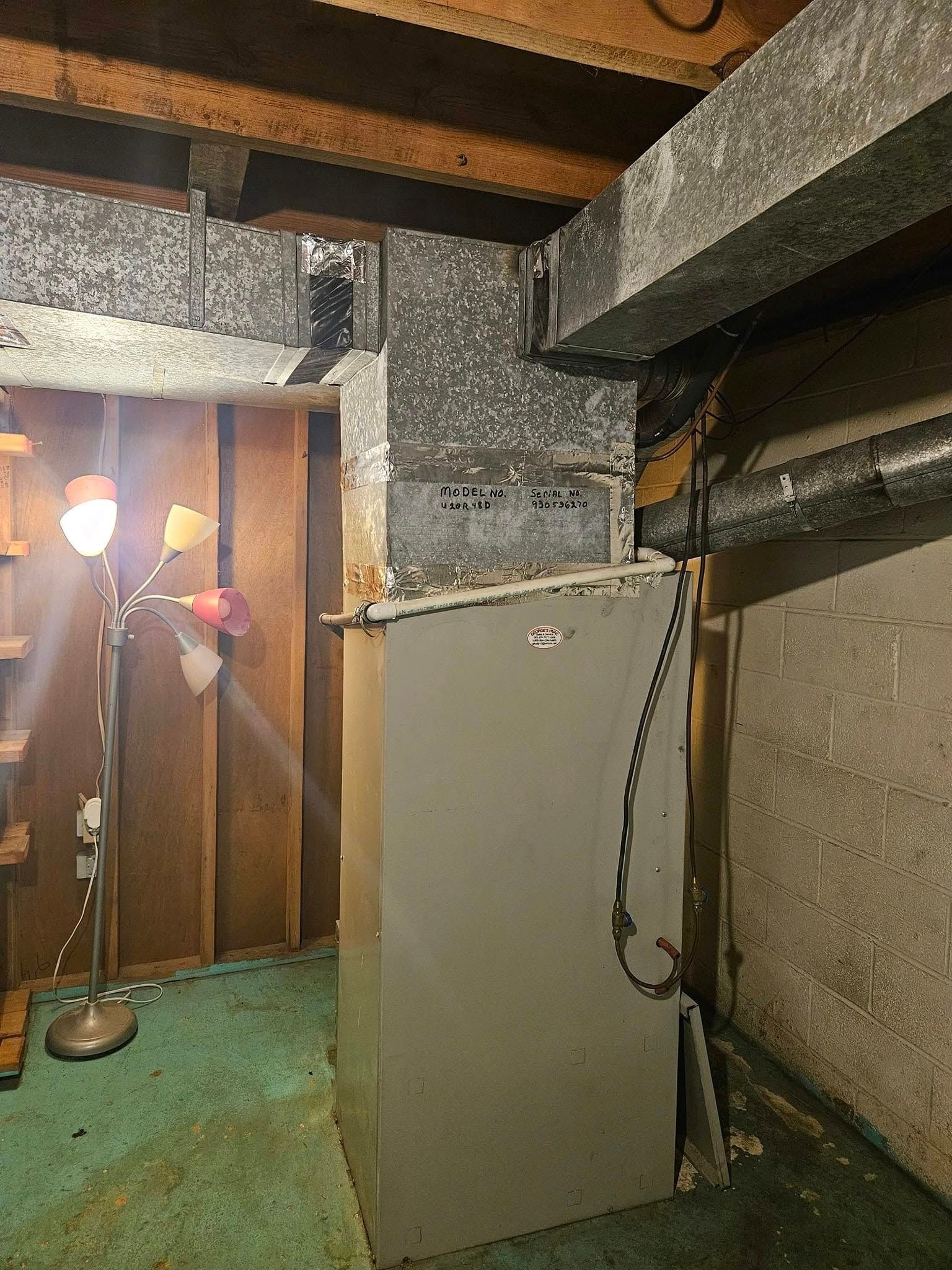 Furnace in a basement, surrounded by ductwork, wood paneling, and a floor lamp.