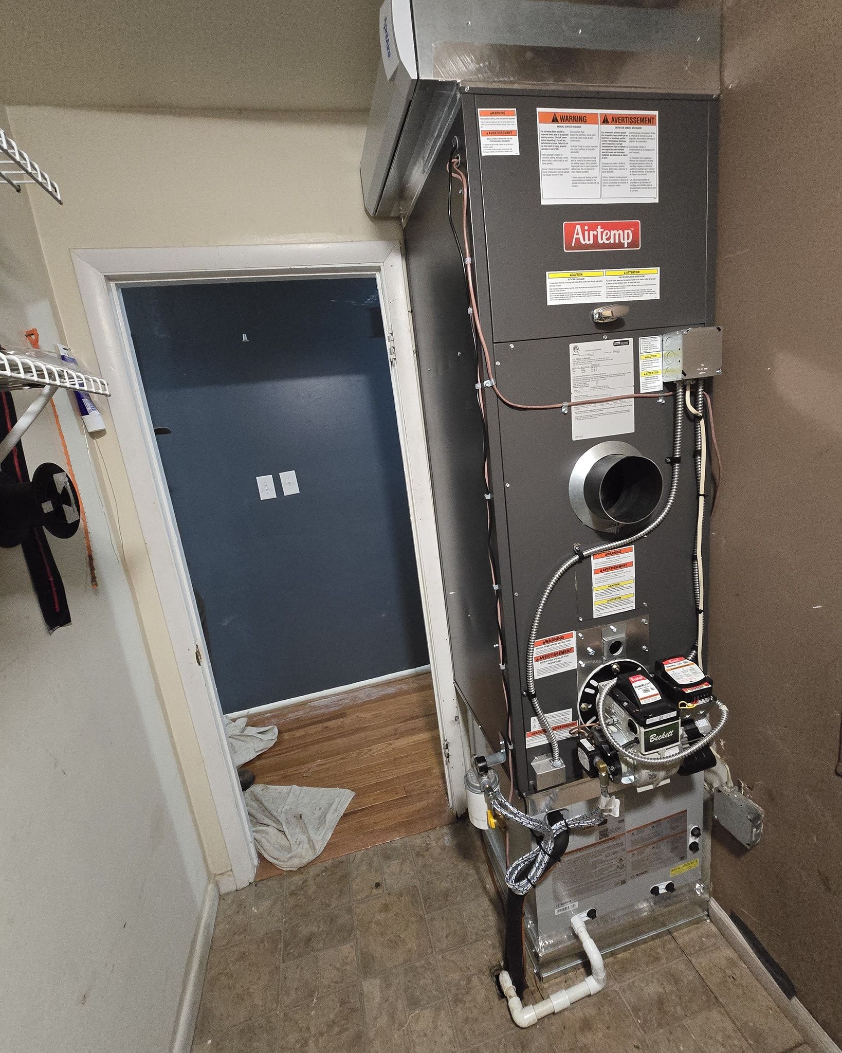 Furnace unit in a utility room. Gray metal with various components, next to a blue door.