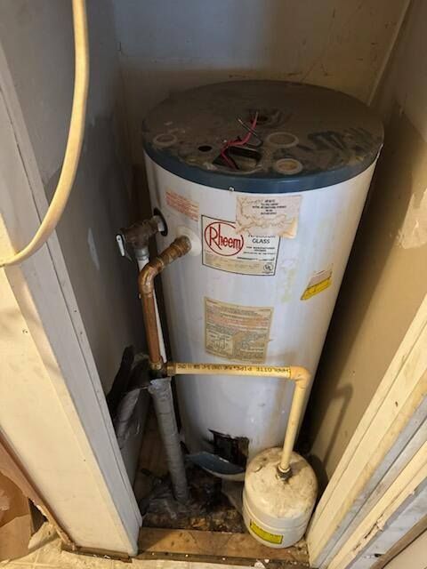 Water heater in a small, enclosed space. It's cylindrical, white, and shows signs of age.