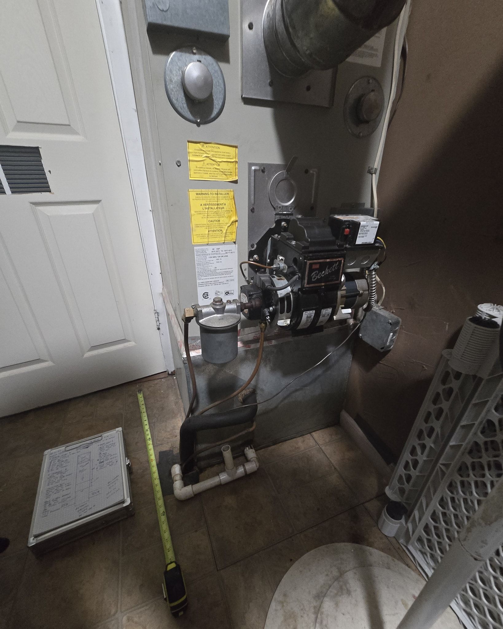 Gas furnace in a utility room. Yellow labels on side. A/C vent on the wall on the left.