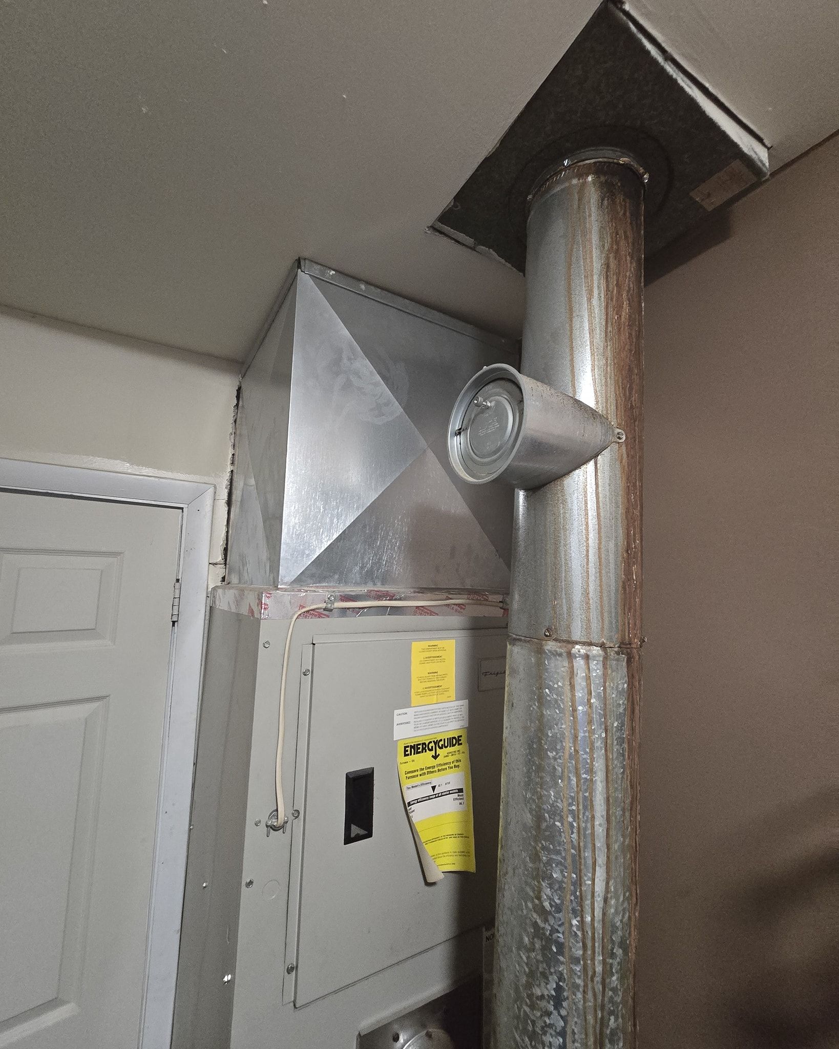 HVAC unit with ductwork in a room. Metal box-shaped unit has a vent connected to a vertical pipe.