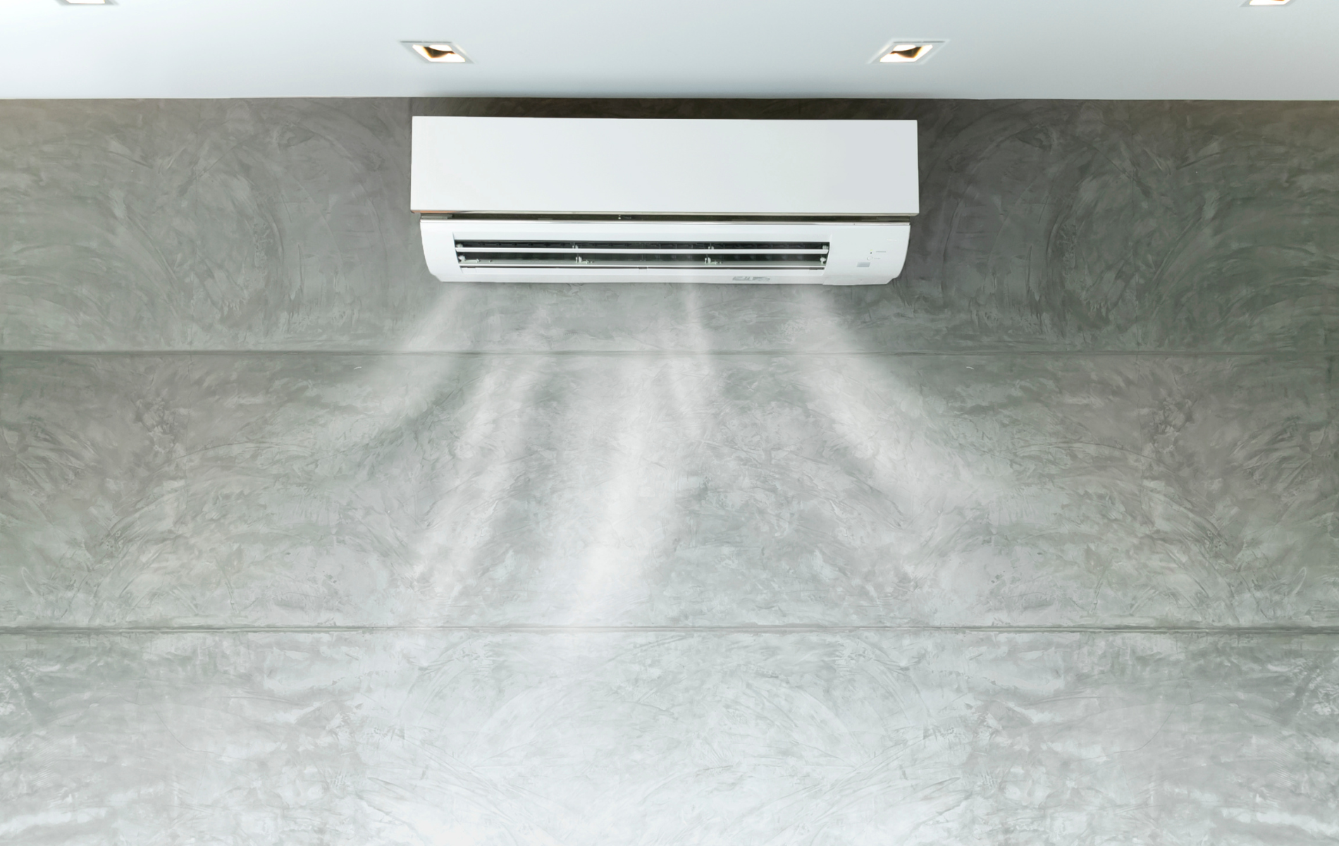 White air conditioner on a gray concrete wall, blowing air downwards.