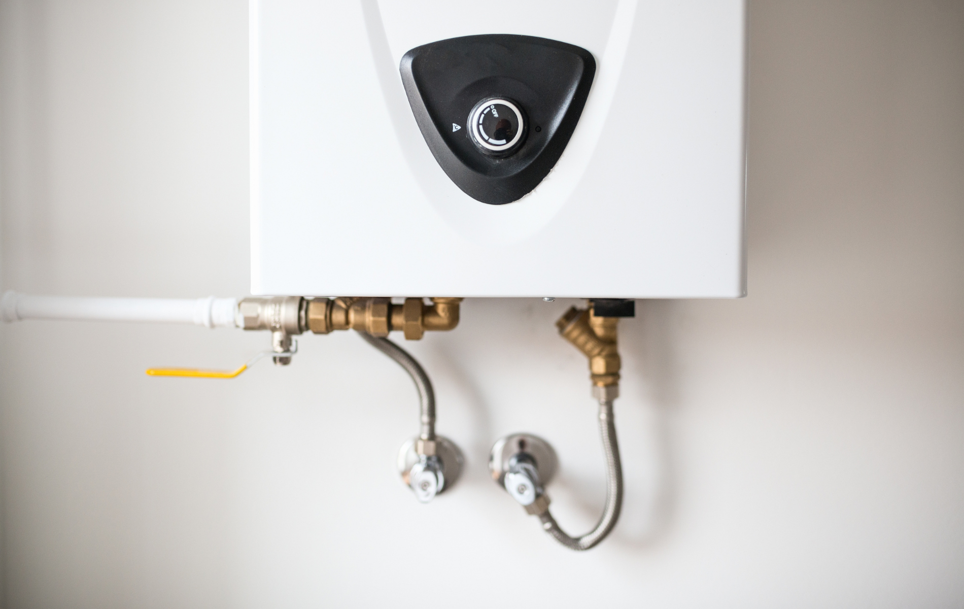 White water heater mounted on a white wall with connected pipes and valves.