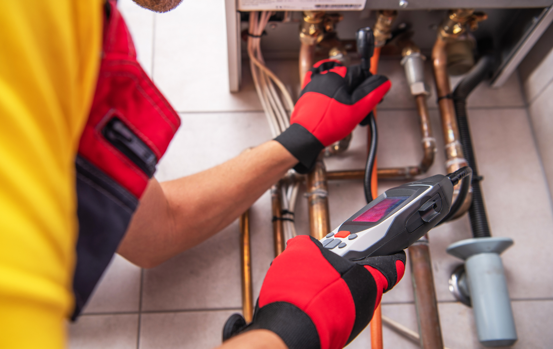 Person inspecting boiler with a device, wearing red gloves.