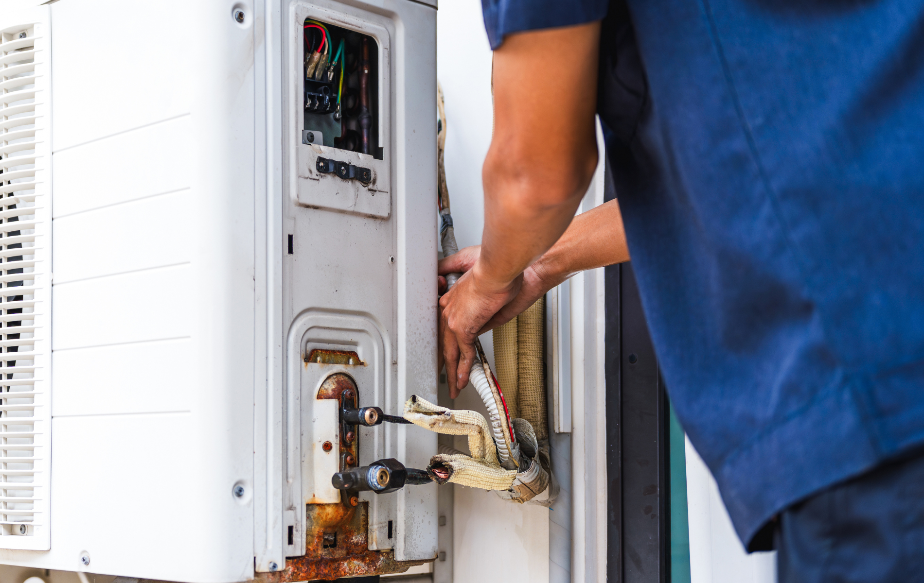 Person in blue shirt repairing an outdoor air conditioning unit.