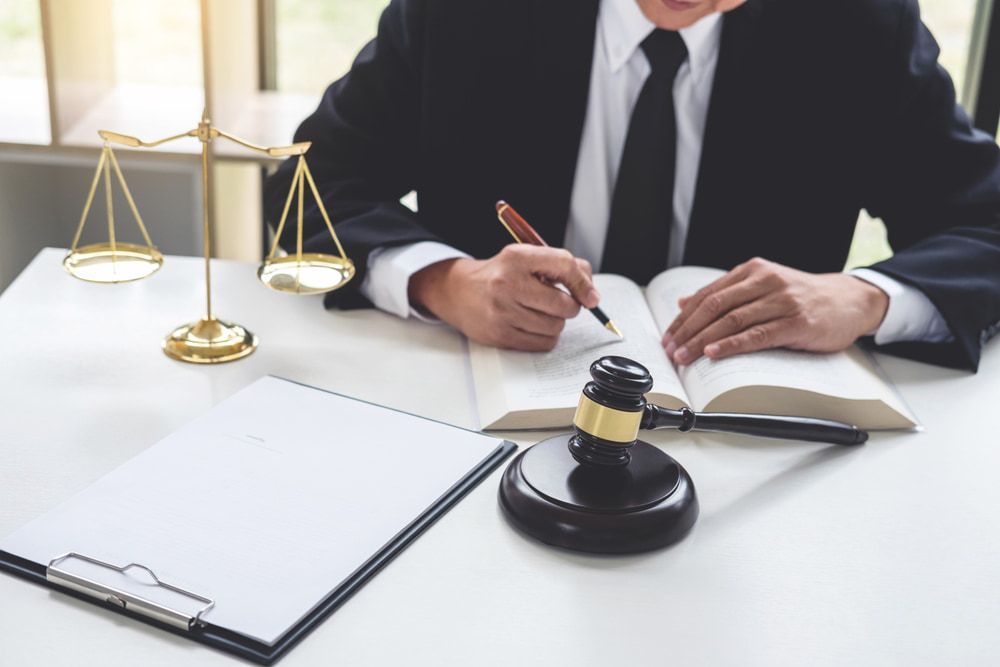 A Man In A Suit And Tie Is Sitting At A Table With A Book And A Gavel — Adamson Legal & Conveyancing in Wingham, NSW