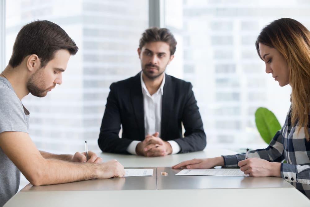 A Man And A Woman Are Sitting At A Table With A Man In A Suit  — Adamson Legal & Conveyancing in Wingham, NSW
