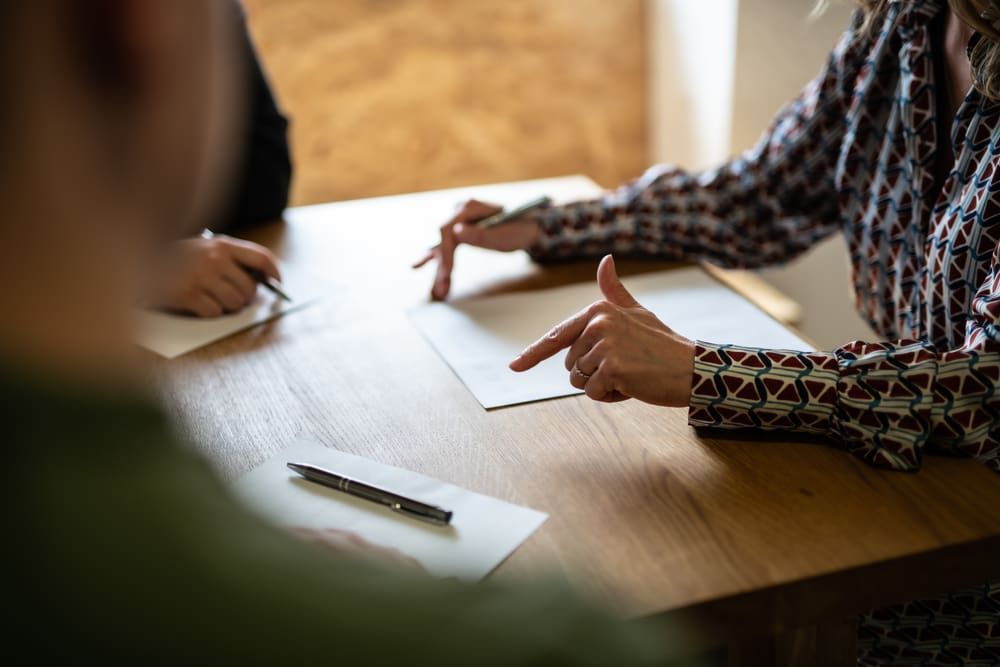 A Woman Is Pointing At A Piece Of Paper While Sitting At A Table — Adamson Legal & Conveyancing in Forster, NSW