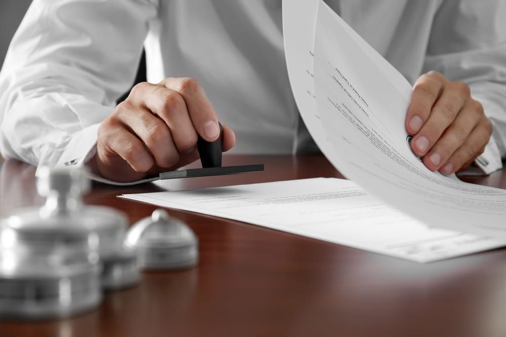 A Man Is Stamping A Document On A Table — Adamson Legal & Conveyancing in Wingham, NSW