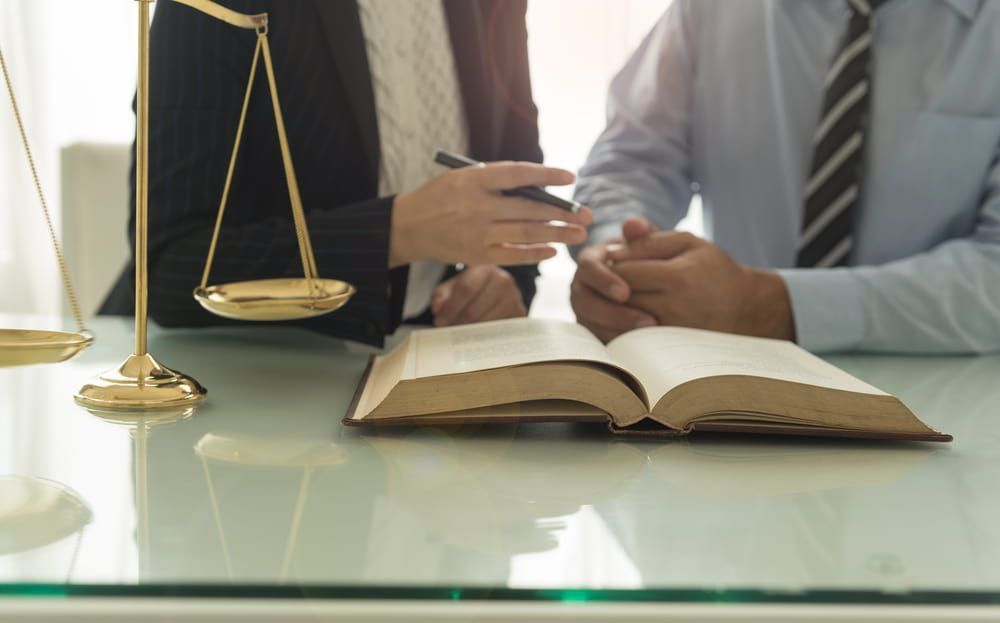 Two Lawyers Are Sitting At A Table With A Book And Scales Of Justice — Adamson Legal & Conveyancing in Wingham, NSW