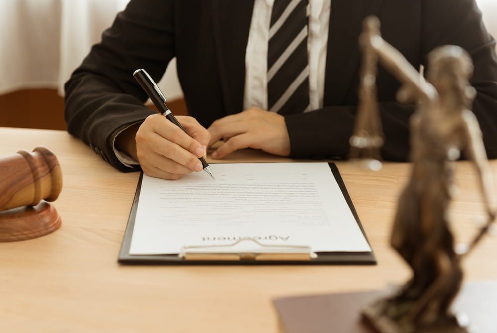 A Man In A Suit And Tie Is Signing A Document — Adamson Legal & Conveyancing in Wingham, NSW