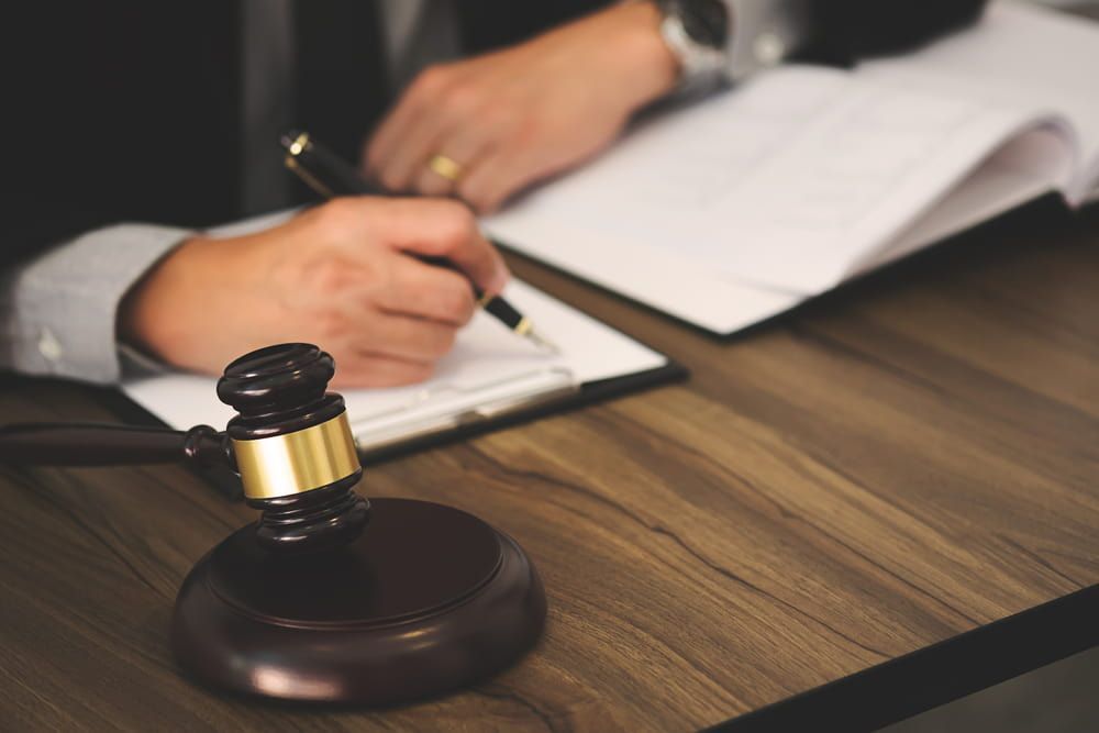 A Person Is Writing On A Clipboard Next To A Judge 's Gavel — Adamson Legal & Conveyancing in Wingham, NSW