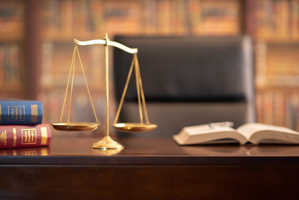 A Scale Of Justice Is Sitting On A Wooden Desk Next To A Stack Of Books — Adamson Legal & Conveyancing in Wingham, NSW