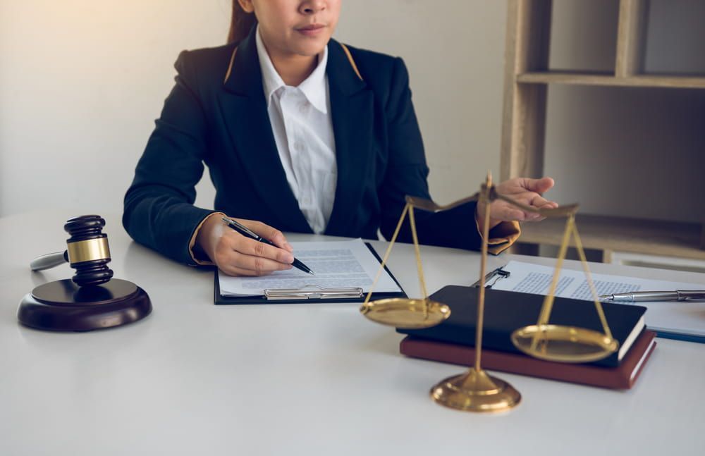 A Female Lawyer Is Sitting At A Desk With A Gavel And Scales Of Justice — Adamson Legal & Conveyancing in Wingham, NSW