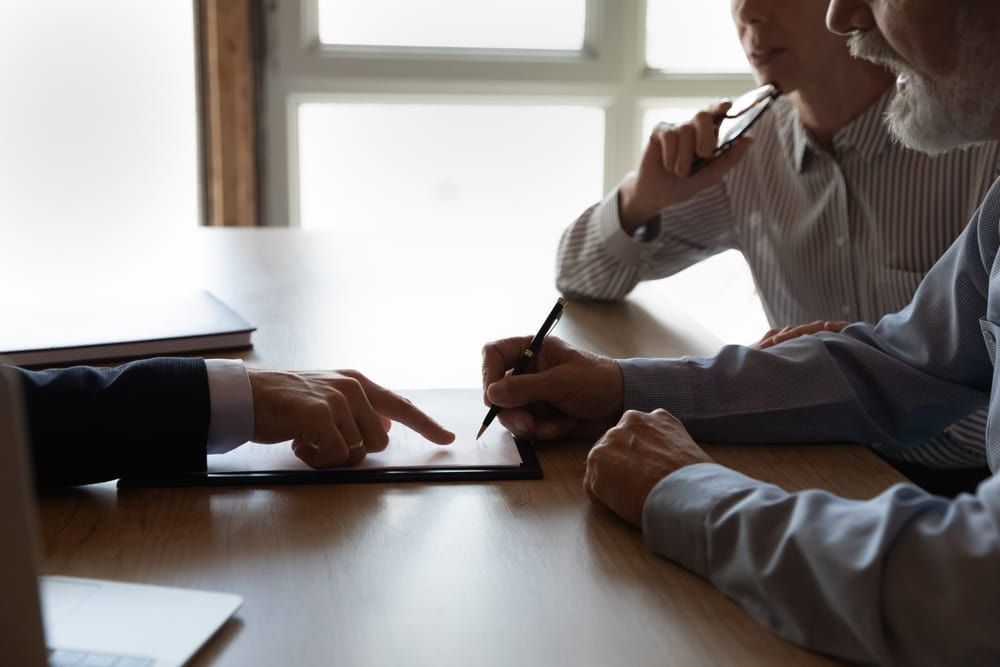 Two Men Are Sitting At A Table Looking At A Tablet — Adamson Legal & Conveyancing in Wingham, NSW
