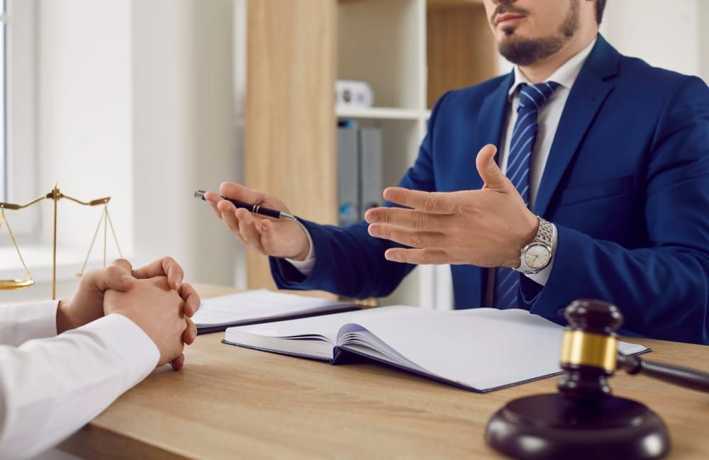 A Man In A Suit And Tie Is Sitting At A Desk Talking To A Woman — Adamson Legal & Conveyancing in Wingham, NSW