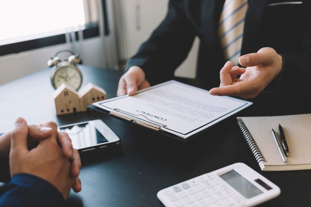 Two Men Are Sitting At A Table Looking At A Piece Of Paper — Adamson Legal & Conveyancing in Forster, NSW