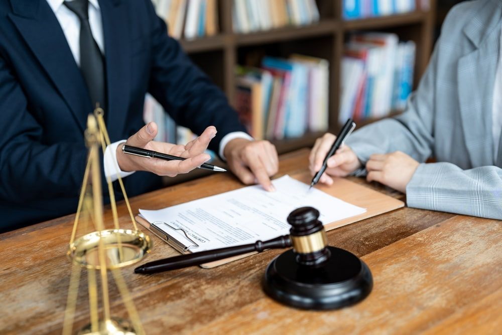 A Man And A Woman Are Sitting At A Table With A Gavel And Scales Of Justice — Adamson Legal & Conveyancing in Wingham, NSW