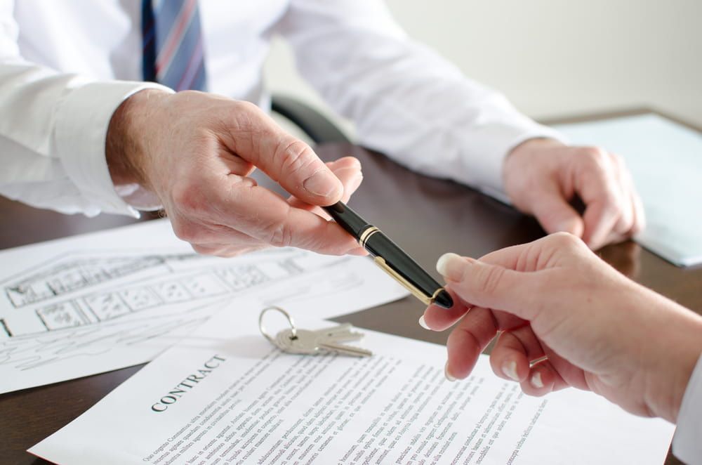 A Man Is Handing A Pen To A Woman Who Is Signing A Contract — Adamson Legal & Conveyancing in Forster, NSW