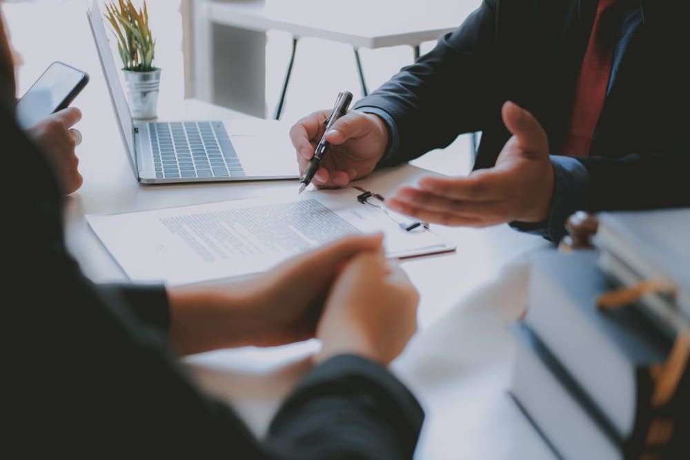 A Man And A Woman Are Sitting At A Table With A Laptop — Adamson Legal & Conveyancing in Wingham, NSW