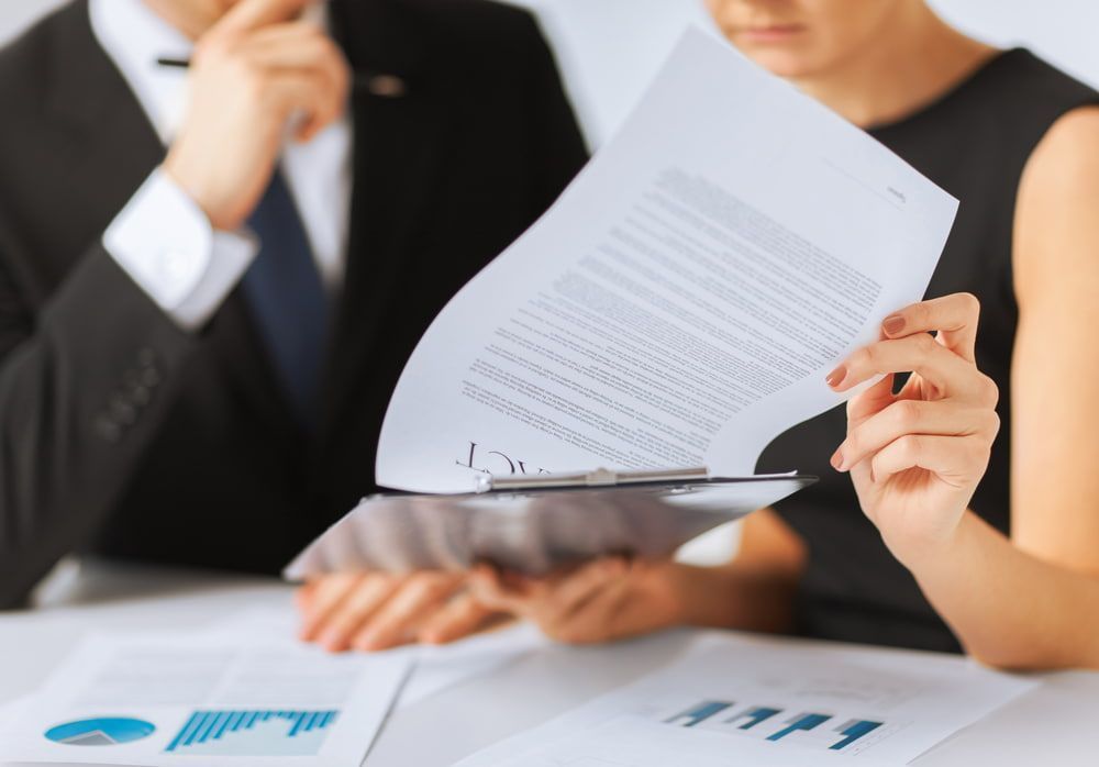 A Man And A Woman Are Sitting At A Table Looking At A Piece Of Paper — Adamson Legal & Conveyancing in Wingham, NSW