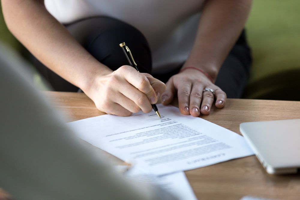 A Woman Is Writing On A Piece Of Paper With A Pen — Adamson Legal & Conveyancing in Wingham, NSW