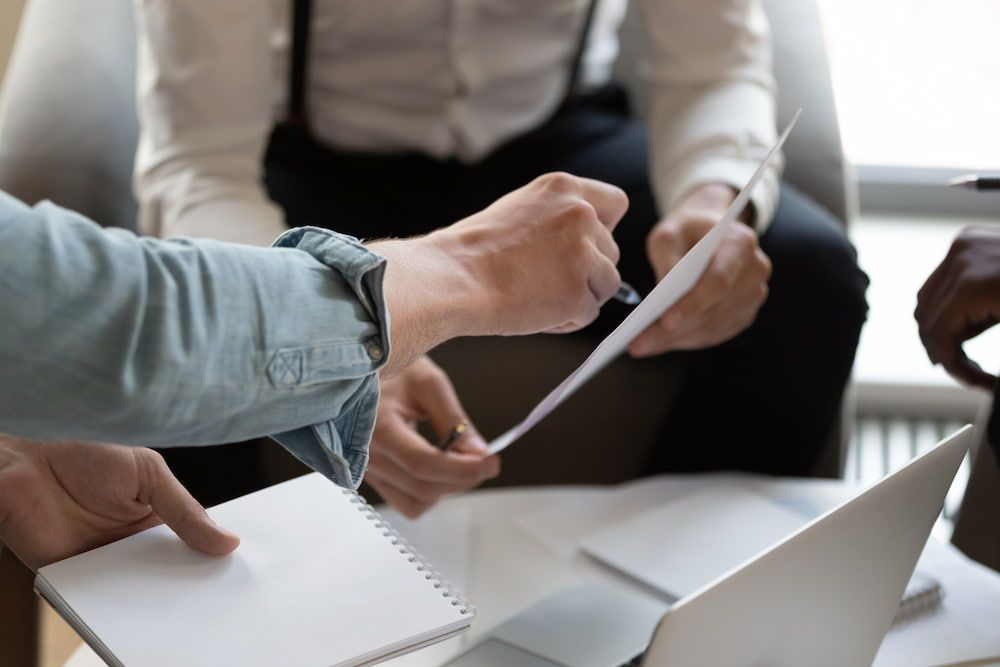 A Group Of People Are Sitting At A Table Looking At A Piece Of Paper — Adamson Legal & Conveyancing in Wingham, NSW