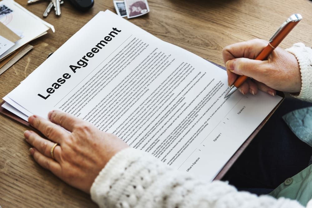 A Person Is Signing A Lease Agreement On A Wooden Table — Adamson Legal & Conveyancing in Wingham, NSW