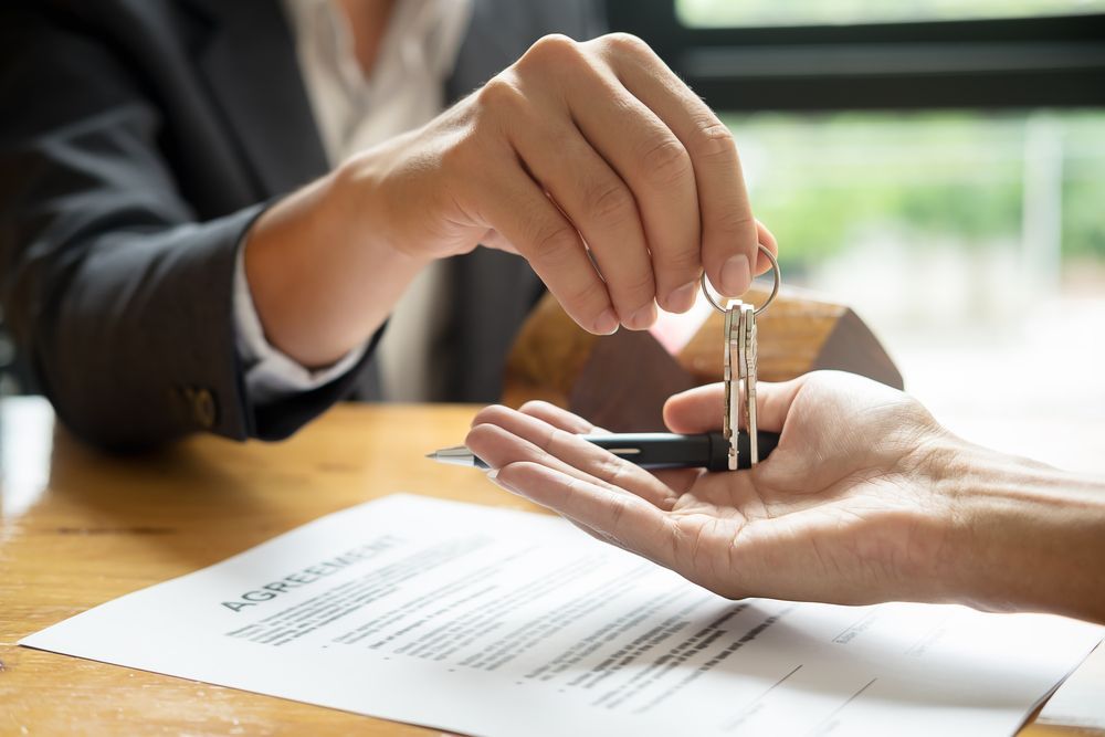 Person Handing Keys to Another Person Over a Loan Document — Adamson Legal & Conveyancing in Wingham, NSW