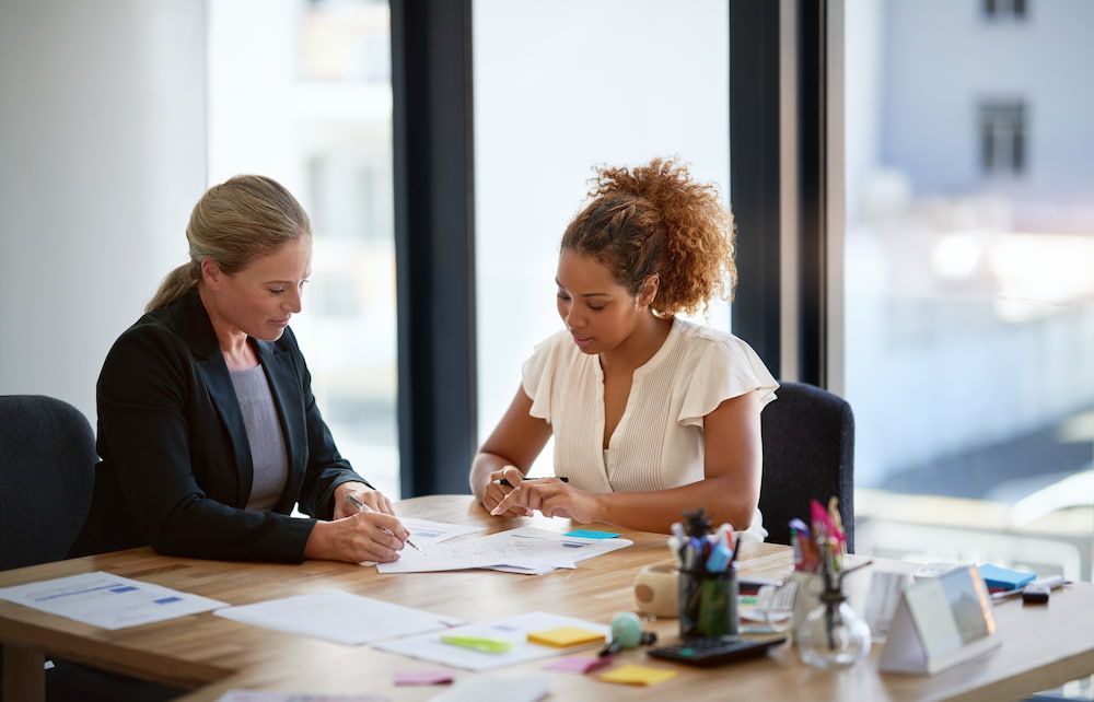 Two Women Are Sitting At A Table Looking At Papers — Adamson Legal & Conveyancing in Wingham, NSW
