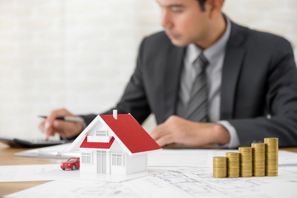 Man in Suit Working on Finances, House Model, Coins, and Car on A Desk — Adamson Legal & Conveyancing in Tamworth, NSW