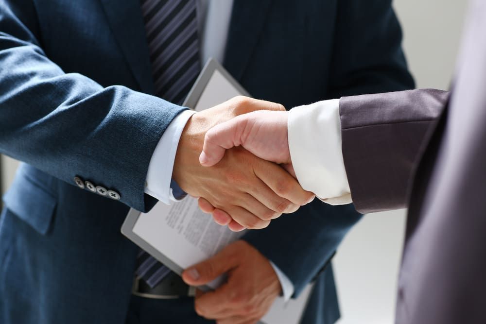 A Man In A Suit And Tie Is Shaking Hands With Another Man — Adamson Legal & Conveyancing in Wingham, NSW