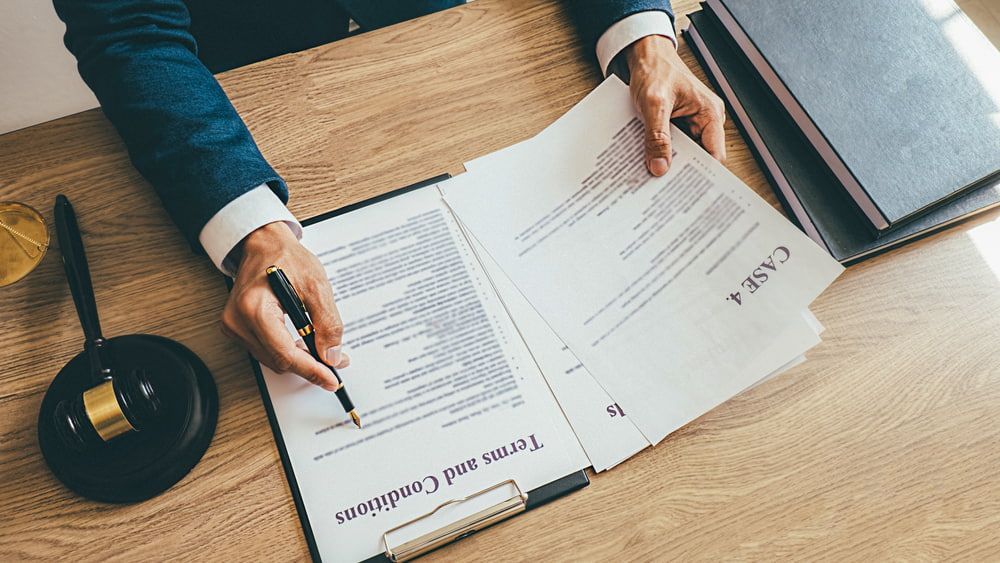 A Man Is Signing A Document On A Clipboard With A Pen — Adamson Legal & Conveyancing in Forster, NSW