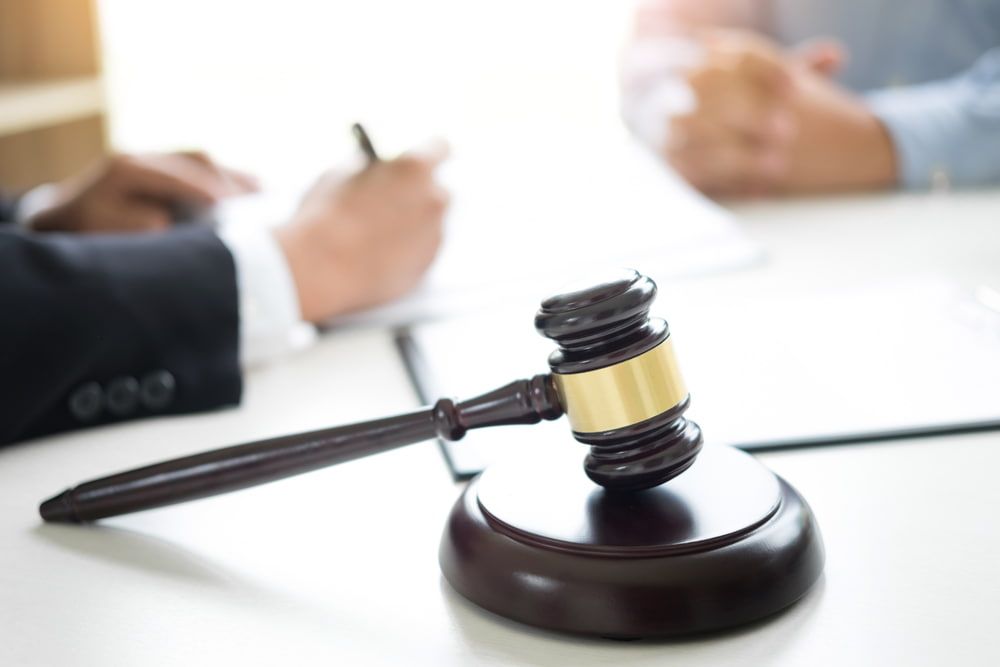 A Judge 's Gavel Is Sitting On A Table Next To A Man In A Suit — Adamson Legal & Conveyancing in Wingham, NSW