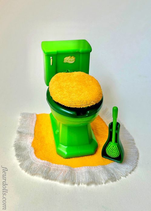 Fleur doll green toilet wc with terrycloth yellow cover on the lid, toilet brush and yellow rug.